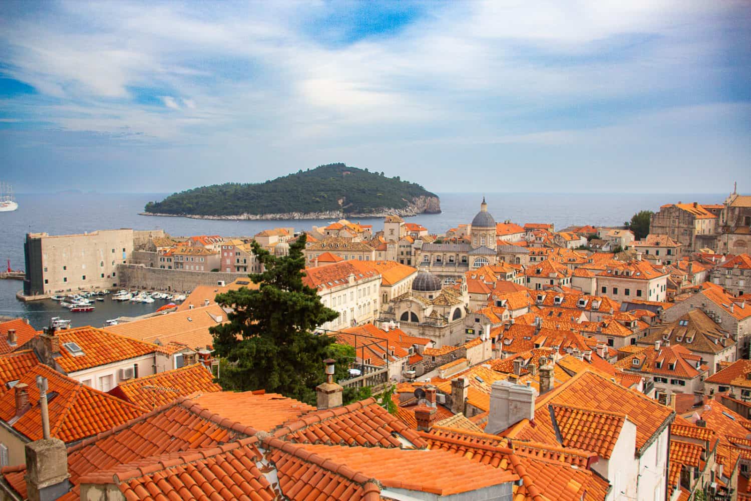 A picture depicting a distant view of Lokrum Island, a popular day trip from Dubrovnik, over the rooftops in Old Town.