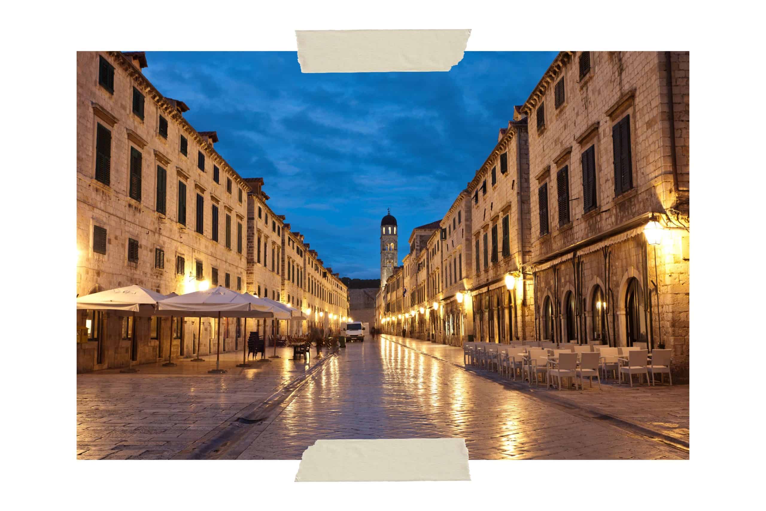 An evening picture of Stradun, the main street running down the center of Old Town Dubrovnik showing buildings lining each side of the street. The sidewalks are illuminated by lanterns. Roaming the streets at night is a must if you only have one day in Dubrovnik.