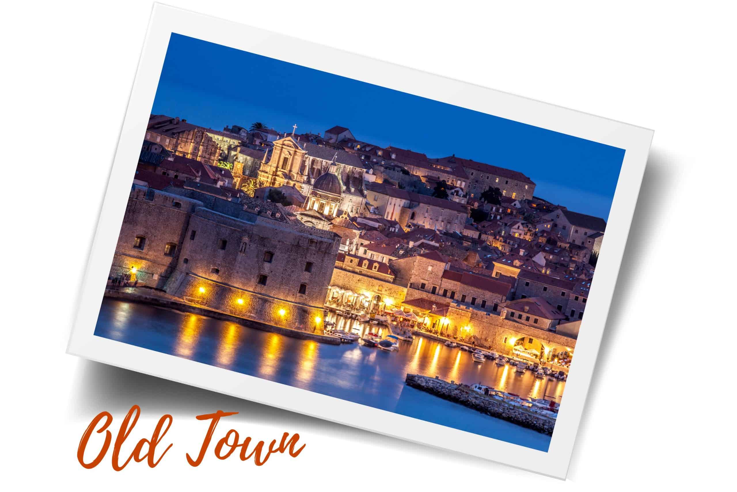 A picture of a nighttime view of Old Town Dubrovnik taken from the water and looking towards the old port. St. John's Fortress is in the foreground and the buildings of Old Town are in the background. The walls are lined with lanterns that are illuminated. If you're wondering where to stay in Dubrovnik, Old Town is the overall best area to stay.
