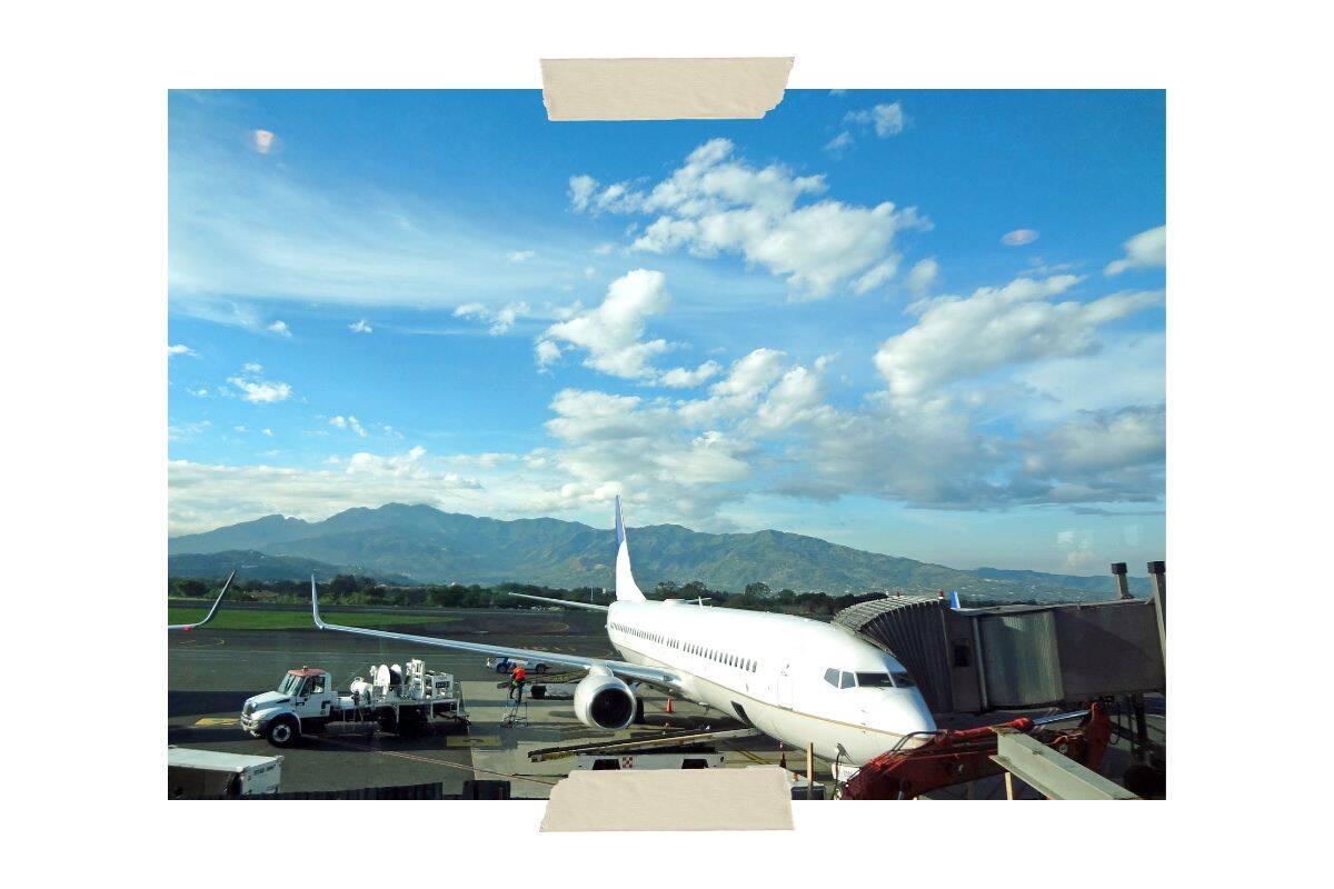 A picture of a white plane sitting at the gate in San Jose, Costa Rica, one of two international Costa Rica airports. There are mountains in the background and a service truck parked next to the plane.