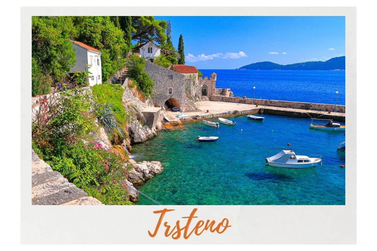 Picturesque stone harbor of Trsteno village with traditional fishing boats in crystal clear Adriatic waters surrounded by Mediterranean vegetation, charming day trip from Dubrovnik