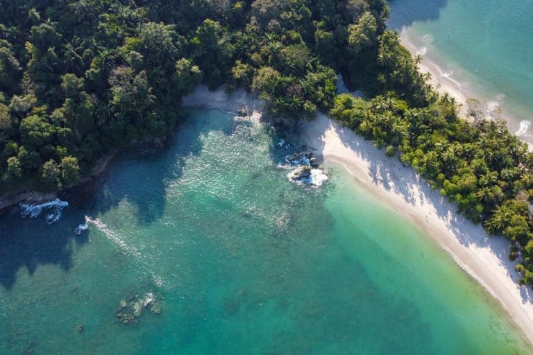 Aerial view of pristine turquoise waters and white sand beach surrounded by lush tropical rainforest during Costa Rica dry season, showcasing perfect weather conditions for beach activities and coastal exploration
