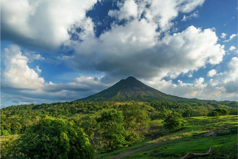 Dramatic cloudy skies over lush green Arenal Volcano and tropical rainforest during Costa Rica rainy season, showcasing vibrant emerald landscapes and dynamic weather patterns typical of green season