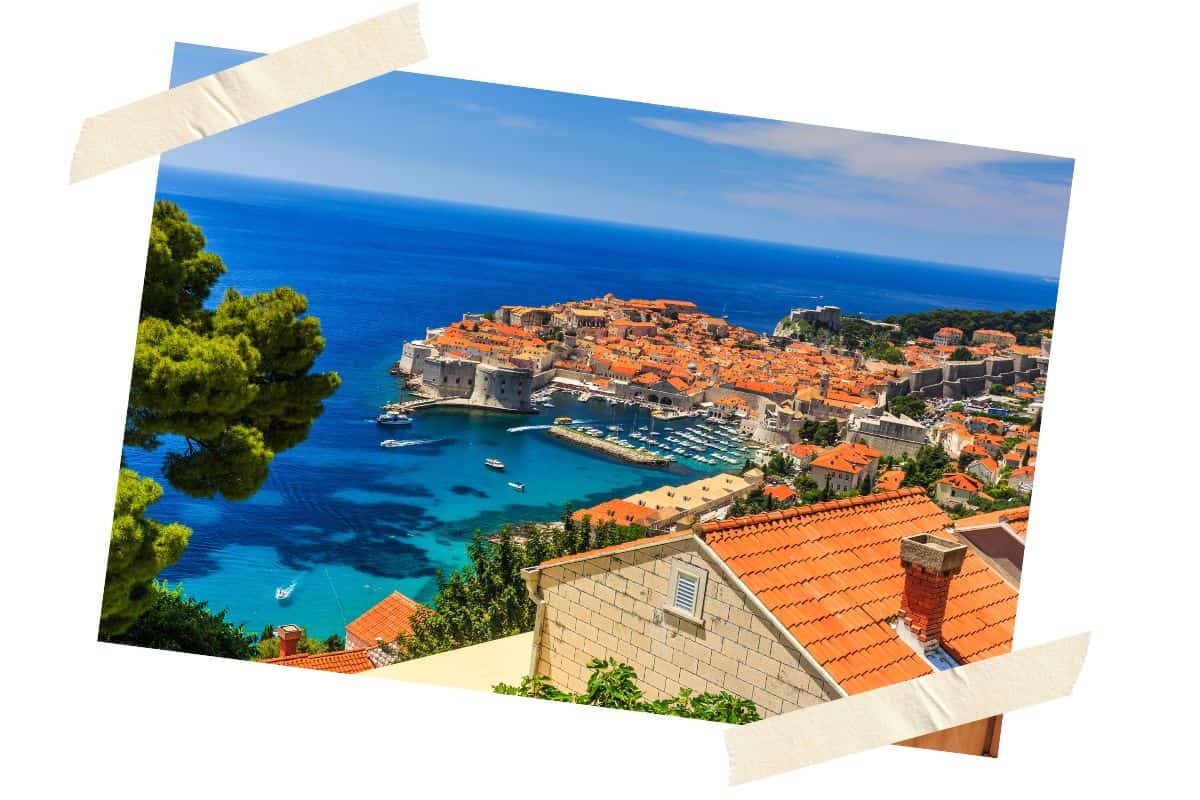 Old Town Dubrovnik in summertime showing red roofed buildings and the turquoise Adriatic waters from a higher elevation.
