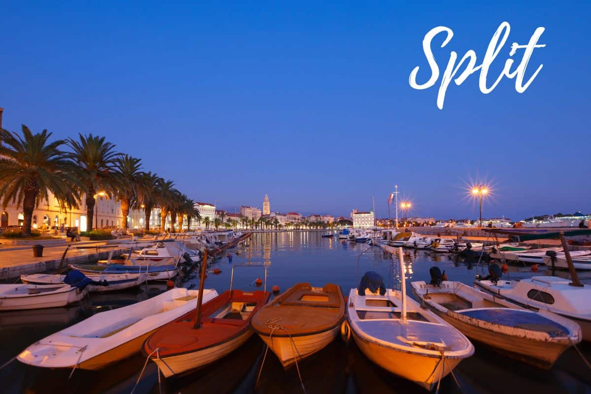 Nighttime in Split, Croatia with boats anchored along the illuminated shoreline. Palm trees and buildings line the walkway along the water.
