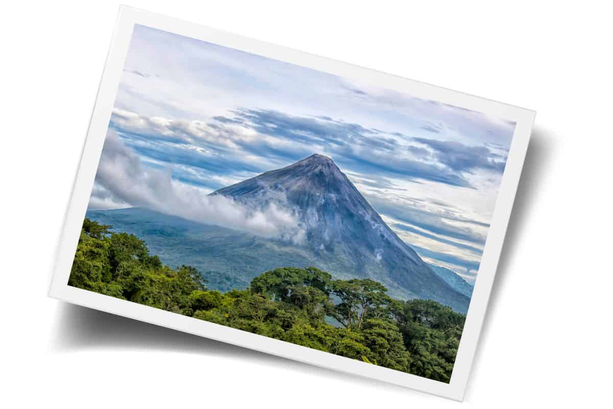 Arenal Volcano cone rising above green jungle with clouds at peak