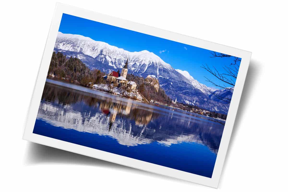 Lake Bled island with church and snow-capped mountains reflected in calm blue water during the best time to visit Slovenia.