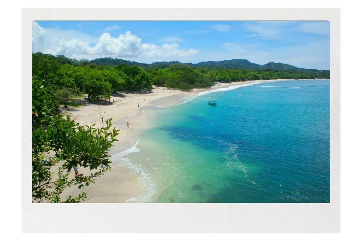 White sand beach with turquoise water and lush green jungle in Costa Rica. A few beachgoers enjoy the pristine coastline under blue skies.