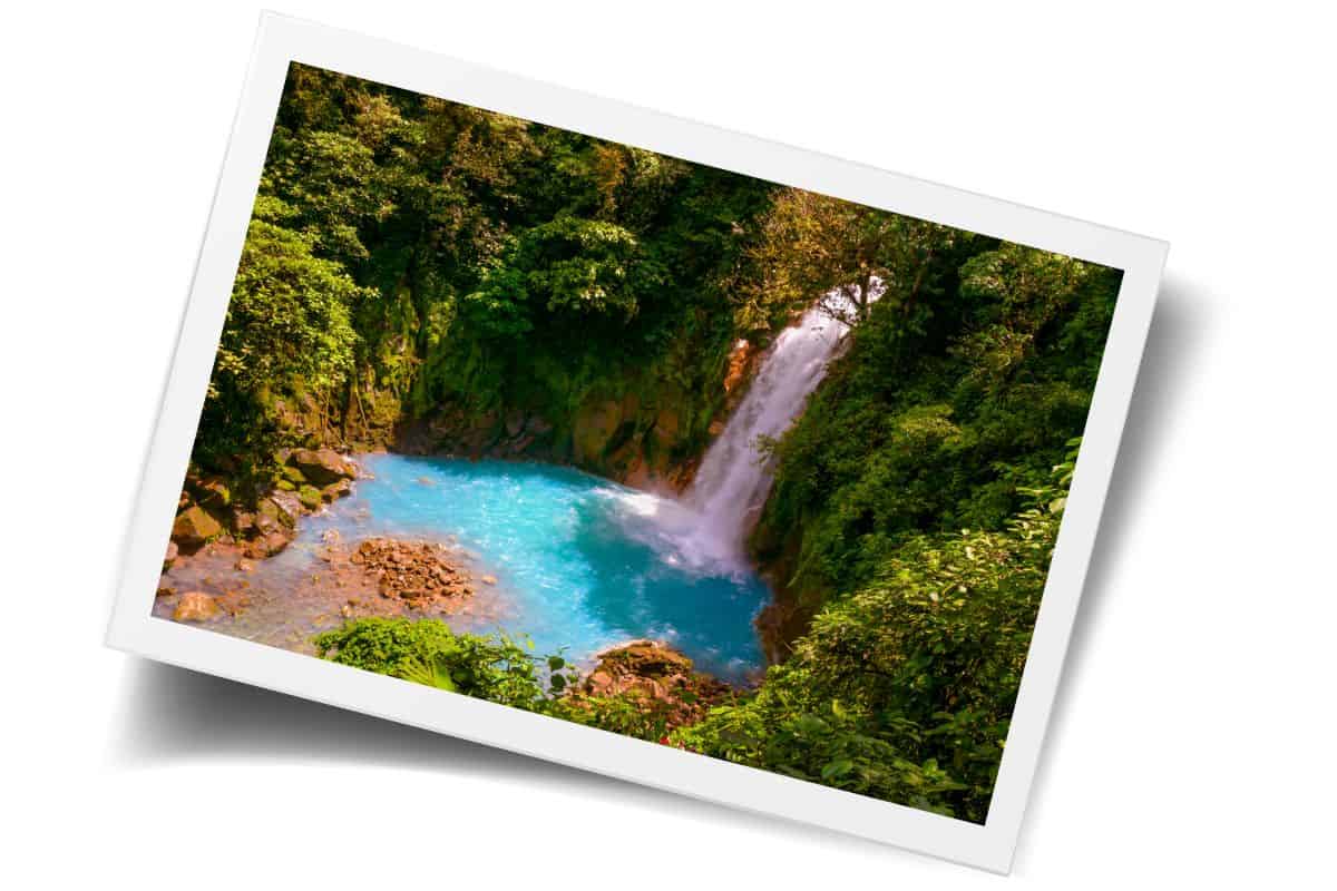 Bright blue waterfall pool surrounded by lush rainforest, cascading into a turquoise basin in Costa Rica.