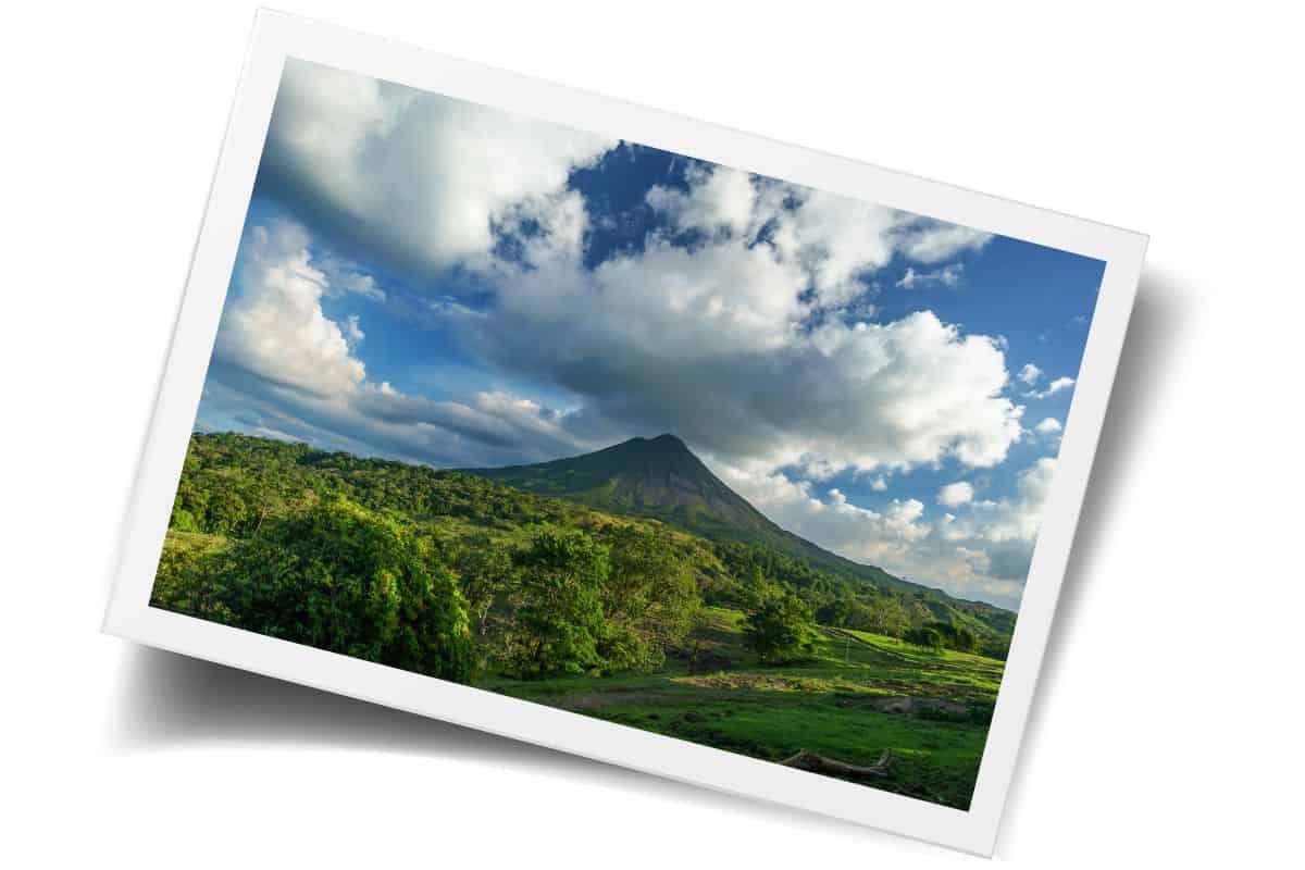 Conical volcano with lush green slopes under dramatic clouds in Costa Rica during rainy season.