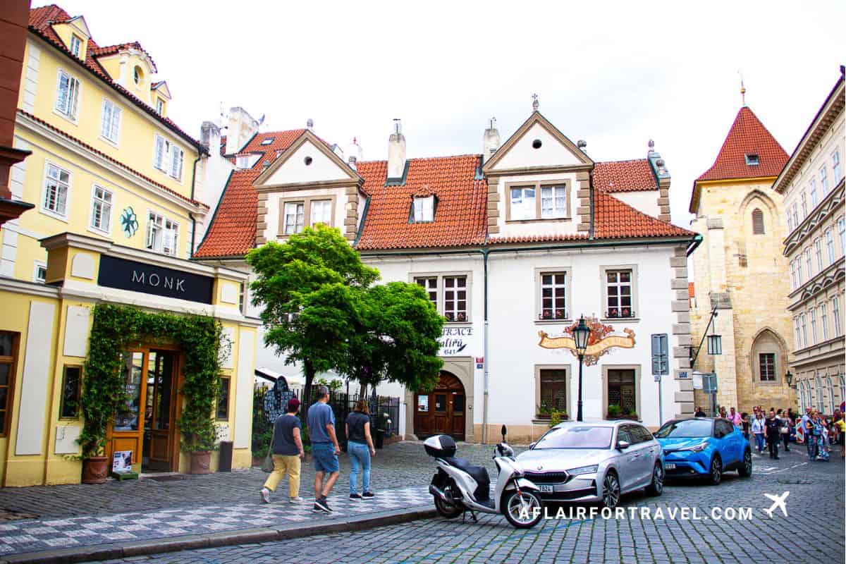 Historic cobblestone street in Prague's Mala Strana neighborhood, just outside the Mandarin Oriental Prague, with colorful buildings featuring red-tiled roofs and traditional Czech architecture