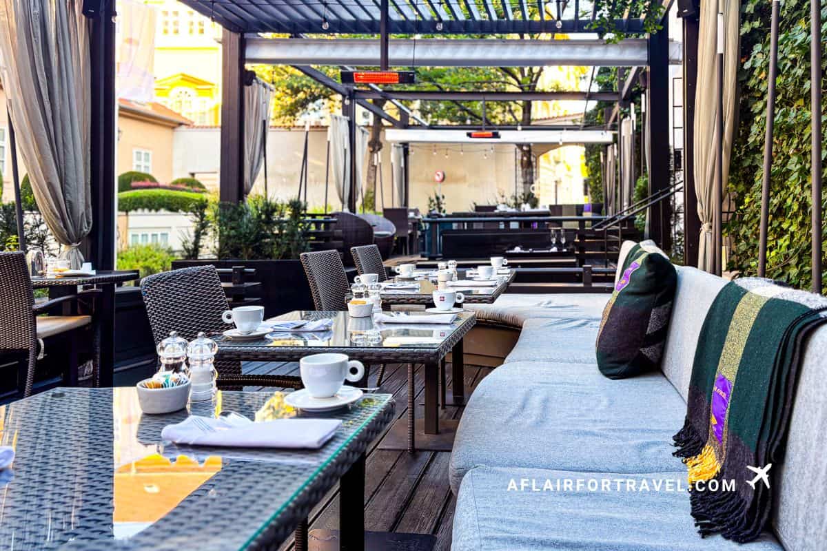 Covered outdoor terrace with comfortable seating, coffee service, and decorative pillows at hotel breakfast area at Mandarin Oriental Prague