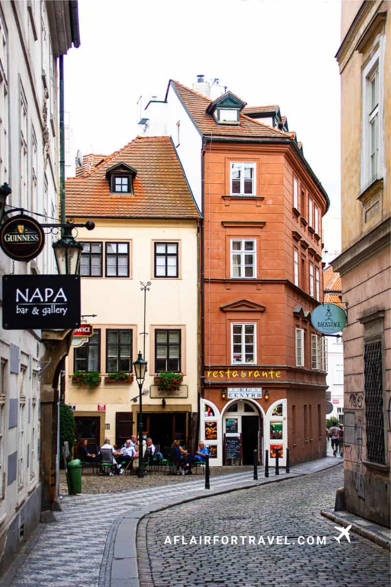 Charming narrow street, just outside Mandarin Oriental Prague, in Lesser Town with colorful buildings, red-tiled roofs, and outdoor cafe seating