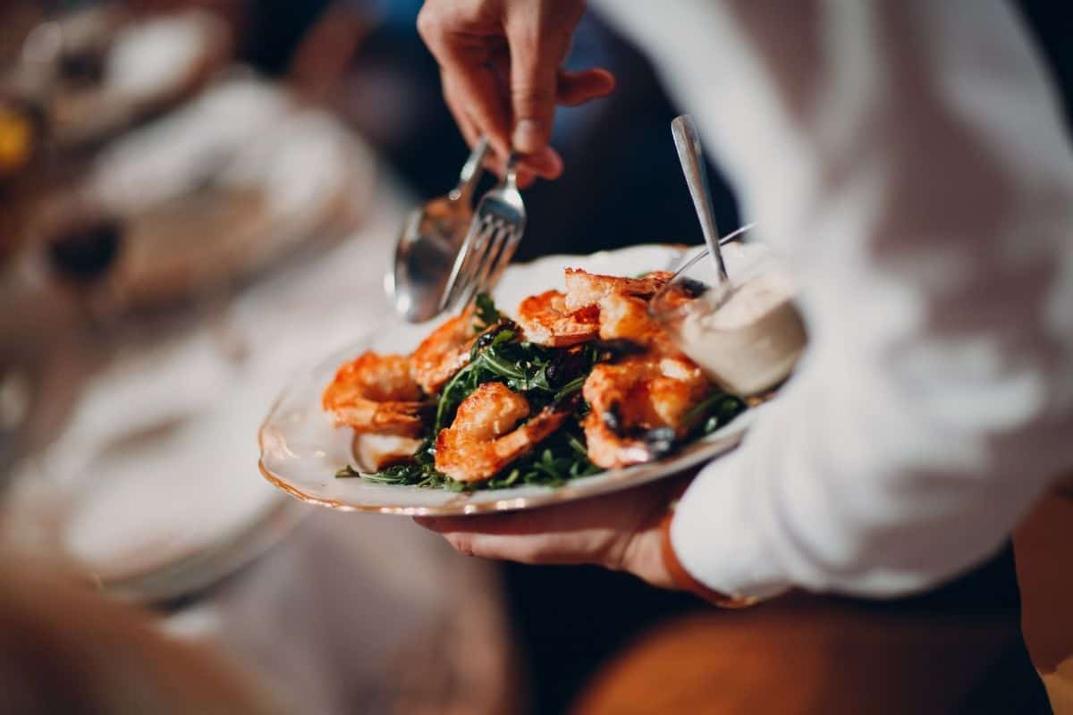 Waiter holding plate of grilled shrimp with greens and cutlery at a restaurant