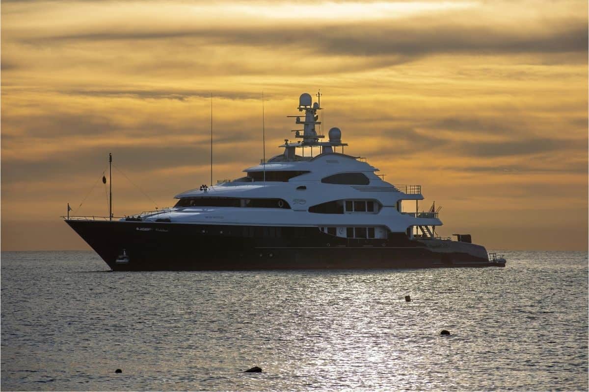Luxury yacht anchored at sea during sunset with golden sky