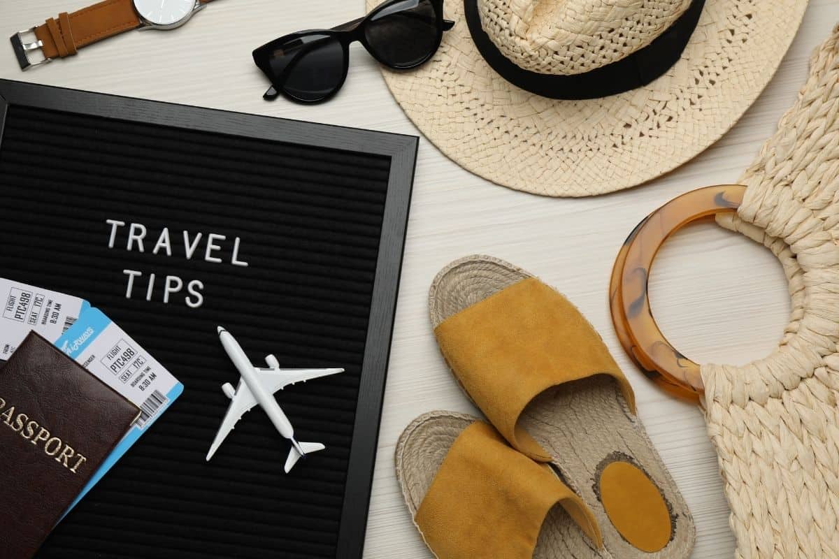 Travel tips letter board with passport, boarding passes, sunglasses, straw hat, sandals, and woven bag on white surface