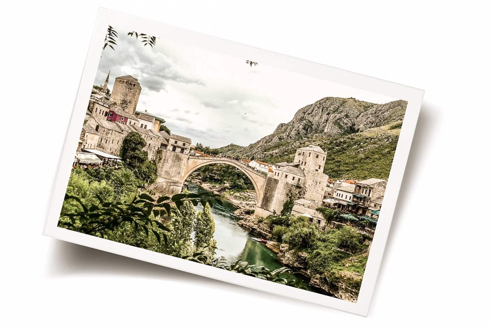 Stari Most (Old Bridge) in Mostar, Bosnia and Herzegovina, spanning the Neretva River with stone buildings and mountains in the background.