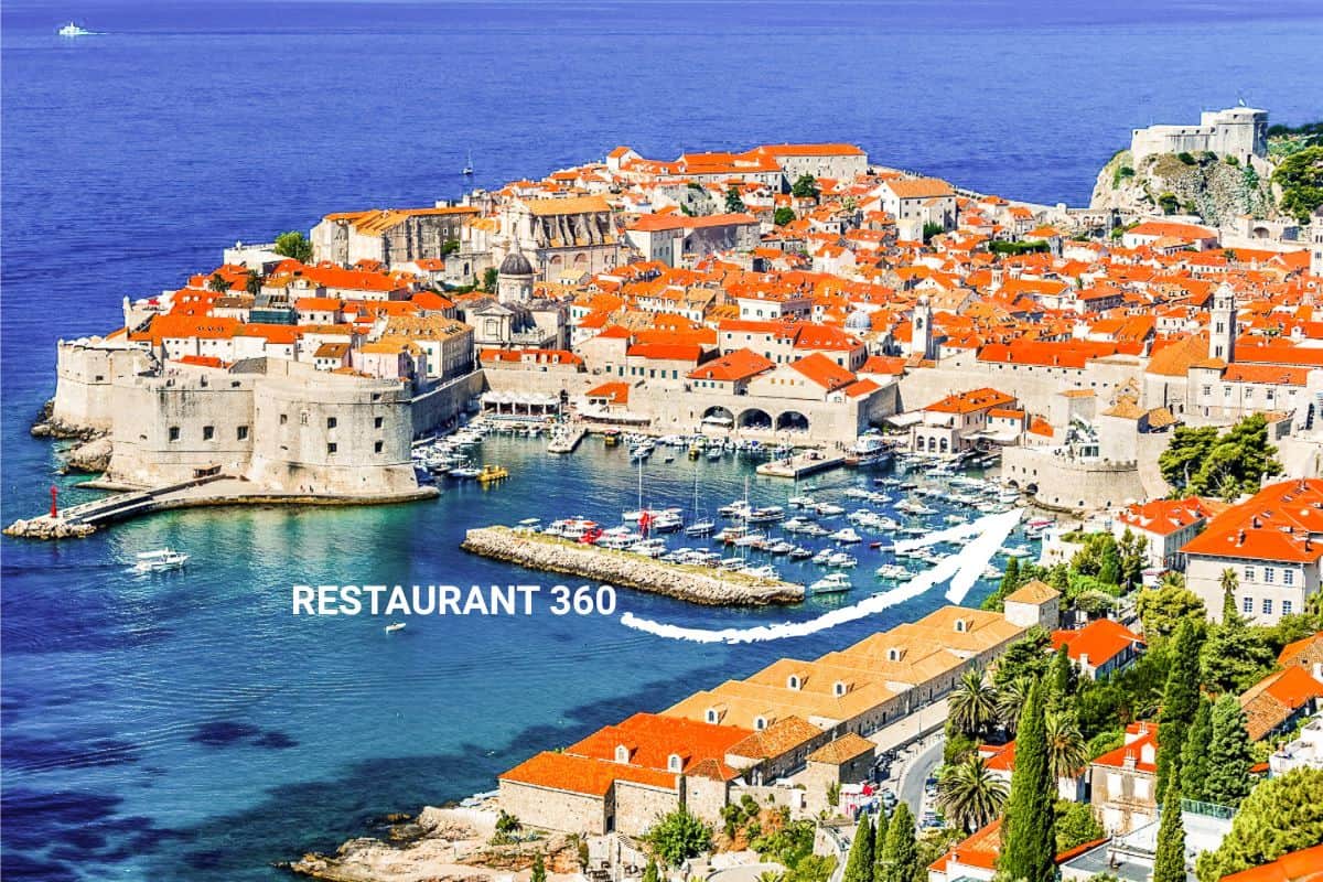 Aerial view of Dubrovnik's old town and harbor with terracotta rooftops, stone fortifications, and boats in turquoise water, with Restaurant 360 marked near the harbor entrance.