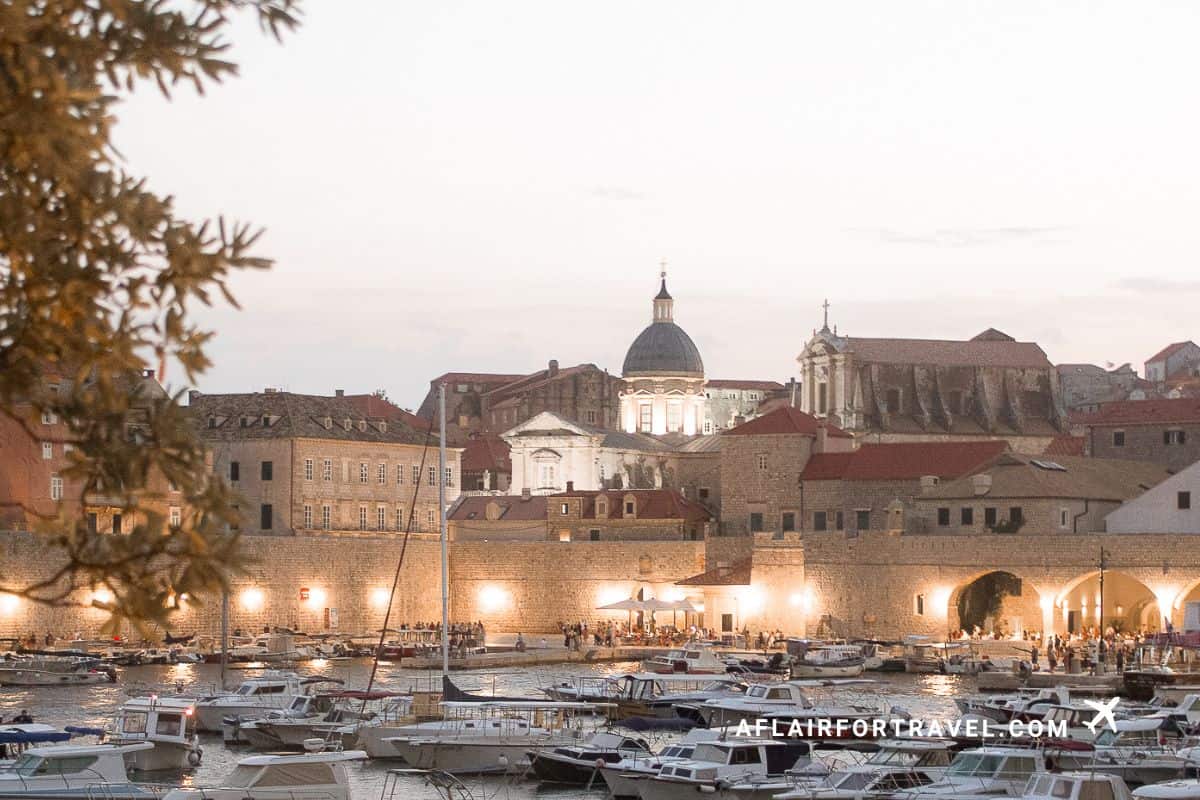 Port 22 Dubrovnik restaurant with a view of the old harbor at sunset, baroque cathedral dome and illuminated city walls with boats