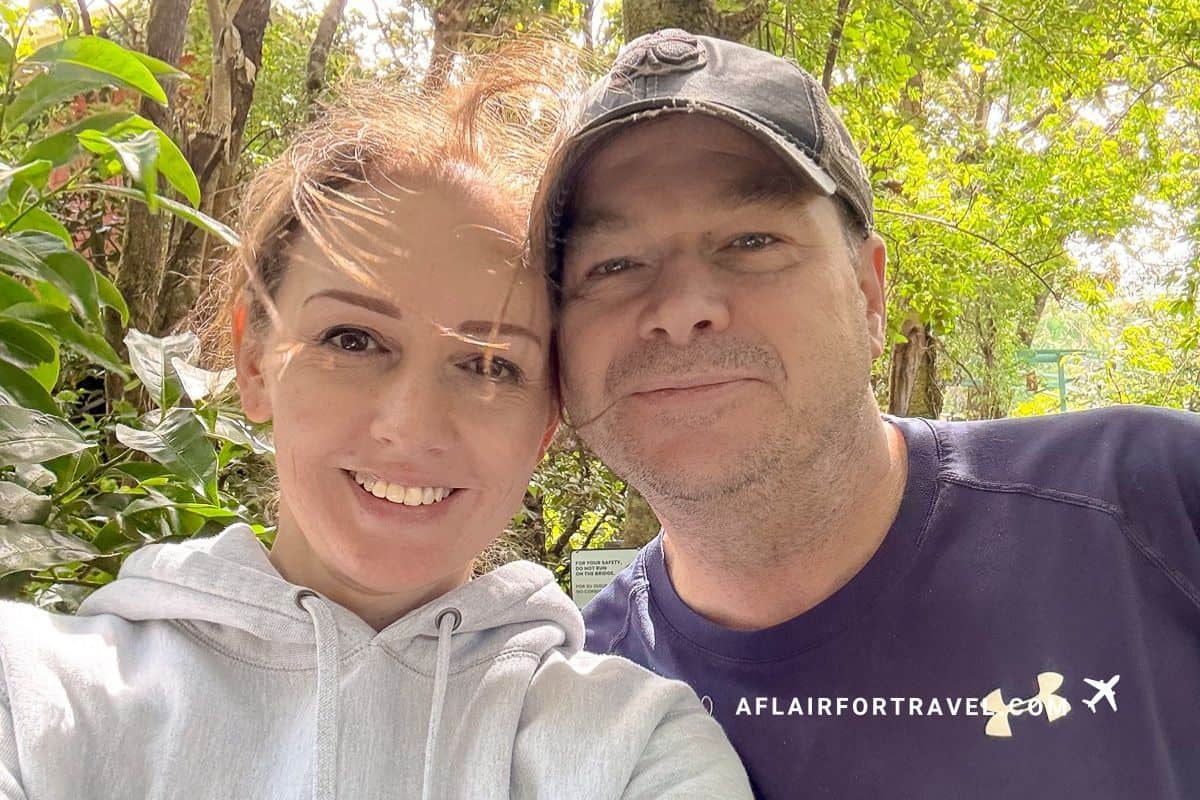 Couple taking selfie in tropical forest setting in Costa Rica, surrounded by lush green vegetation and dappled sunlight