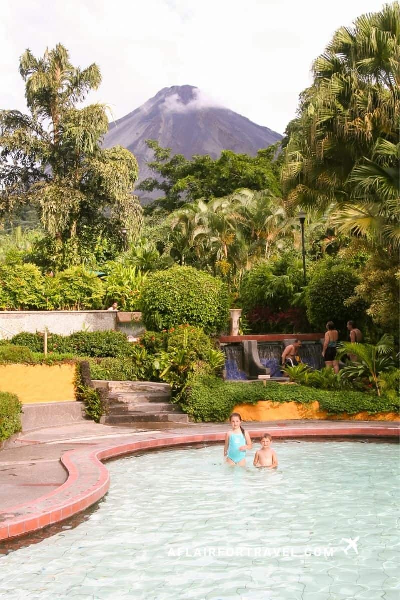 Children playing in an outdoor pool at Tabacón Resort with Arenal Volcano rising in the background, Costa Rica.