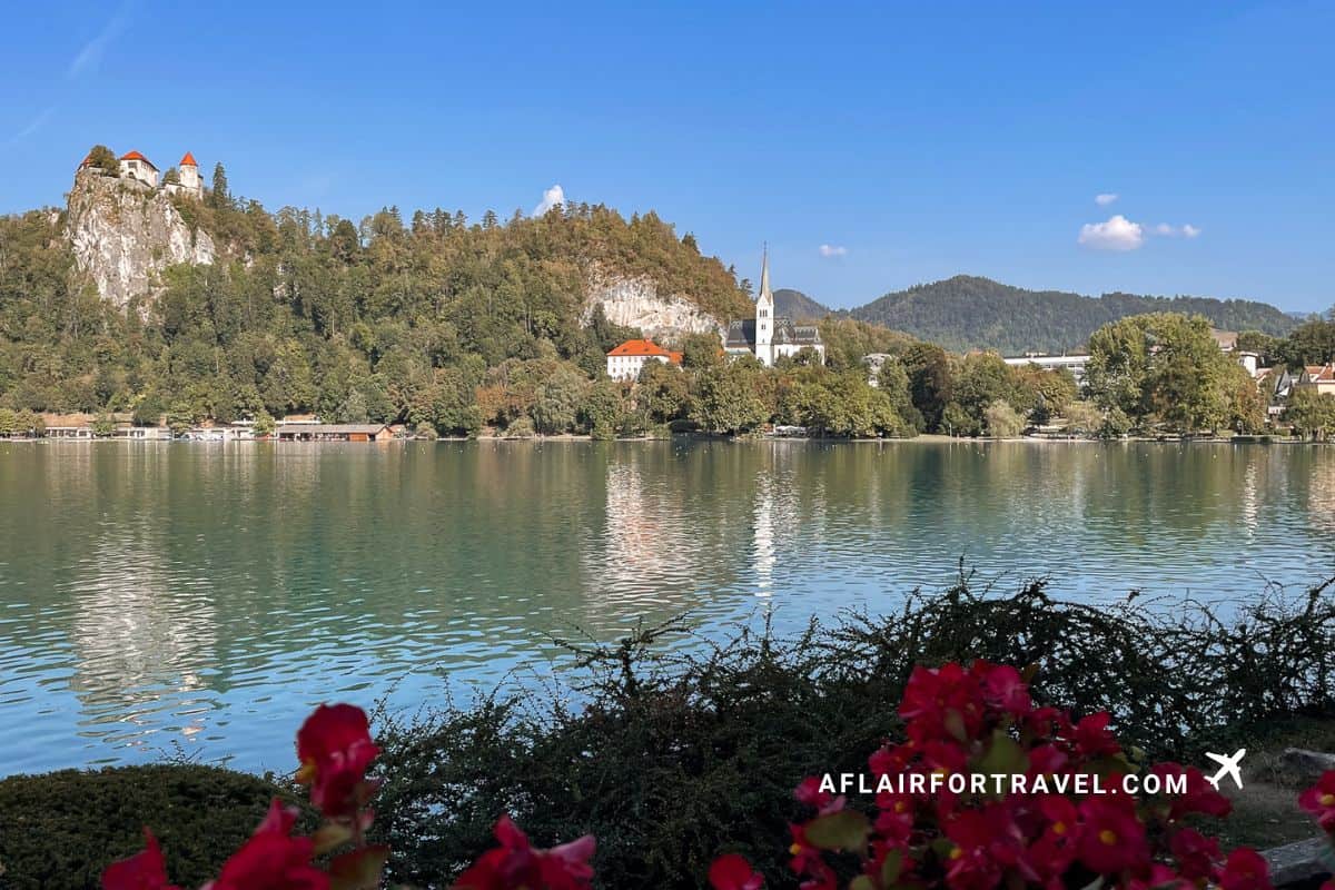 Lakeside view in Lake Bled, with calm turquoise water, forested hills, and Bled Castle on the cliff above.