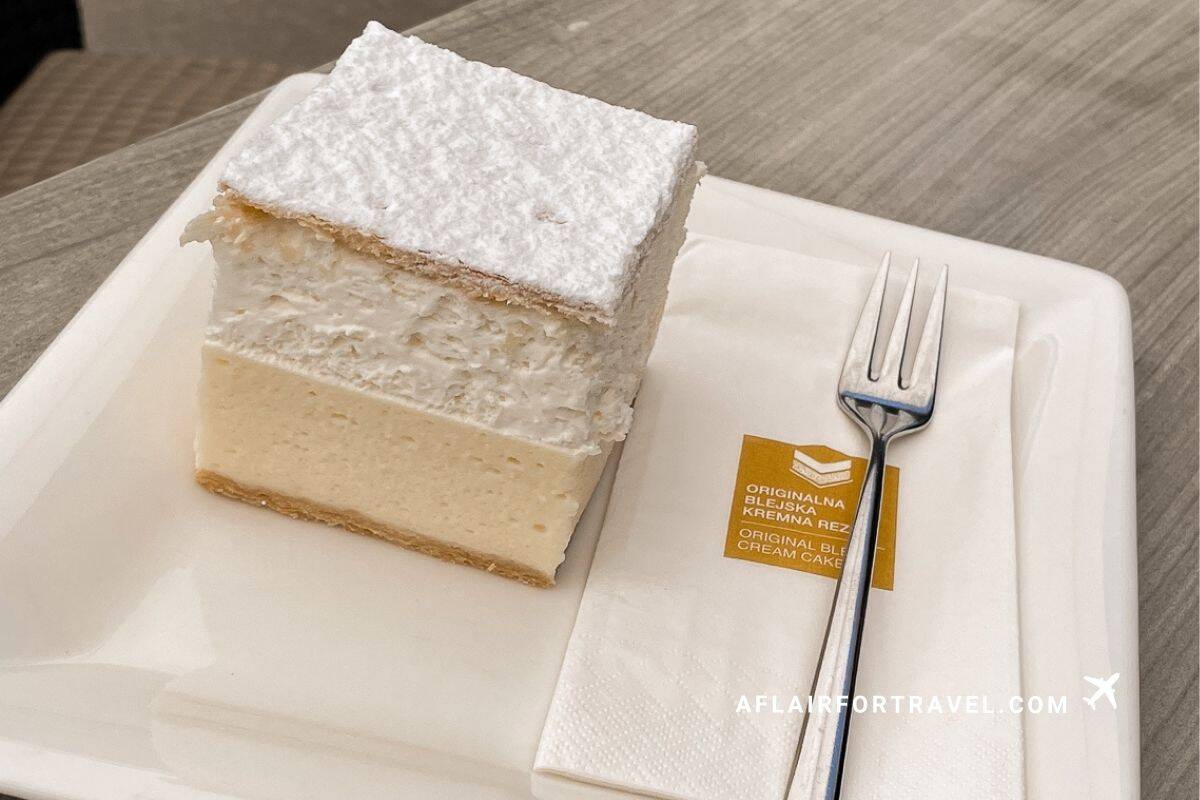 Slice of authentic Bled cream cake (kremna rezina) with layers of vanilla custard, whipped cream, and powdered sugar, a must-try treat during a day in Lake Bled