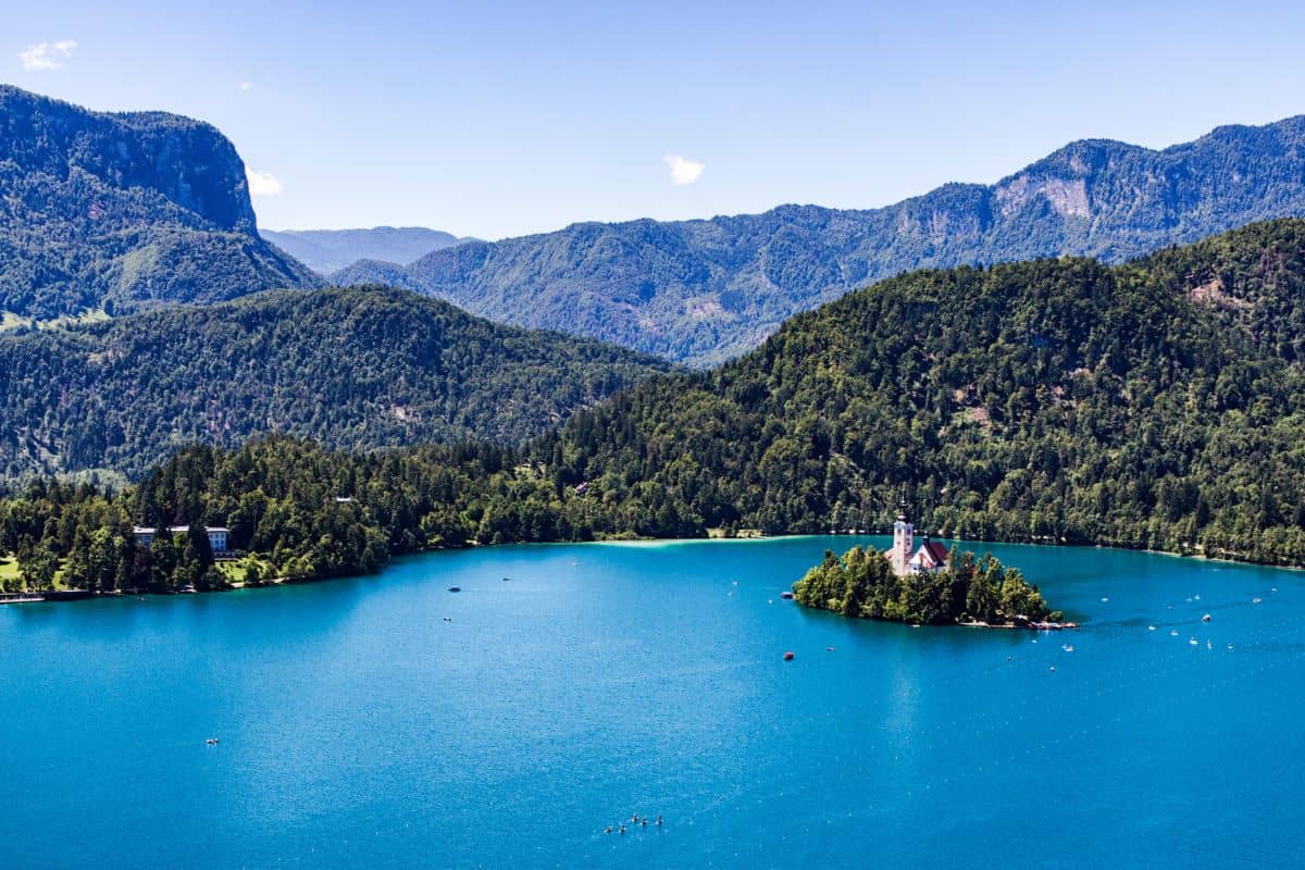 Aerial view of Bled Island with its iconic church surrounded by brilliant turquoise waters, framed by densely forested mountains of the Julian Alps