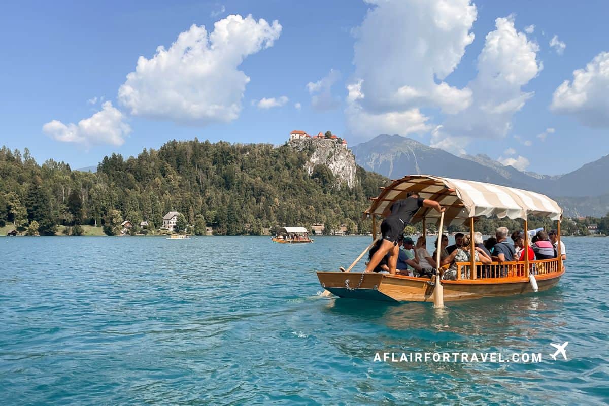 Traditional wooden pletna boat crossing Lake Bled with Bled Castle on the hill in the background