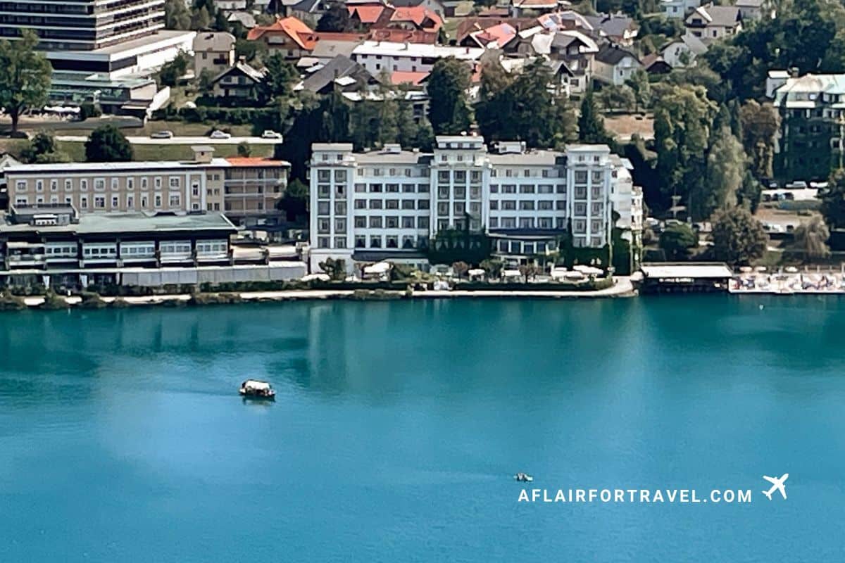 Traditional pletna boat crossing the vibrant turquoise waters of Lake Bled with Grand Hotel Toplice and colorful rooftops in the background