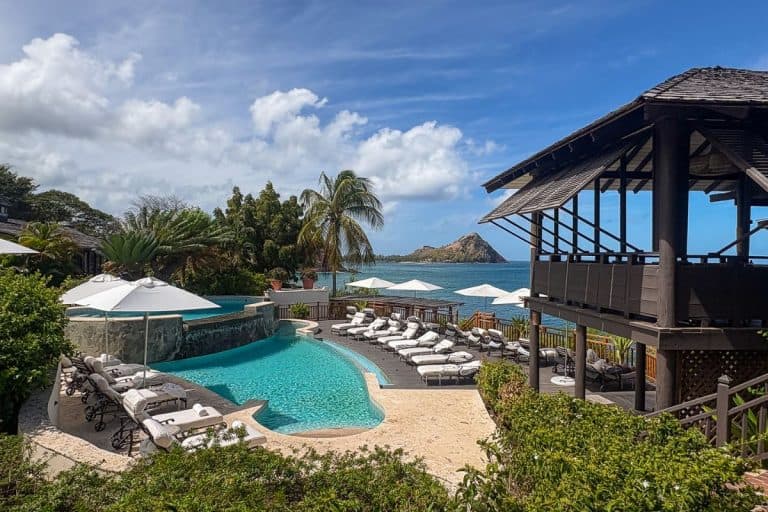 Infinity pool and sun loungers overlooking the turquoise Caribbean Sea at Cap Maison resort in St. Lucia, with a wooden pavilion and Pigeon Island in the distance