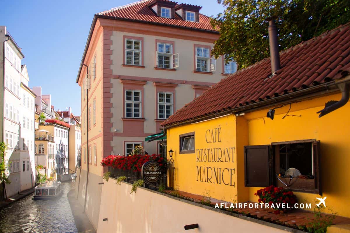 Charming yellow cafe restaurant on Kampa Island, Prague, with red tile roofs, colorful historic buildings, and picturesque canal waterway