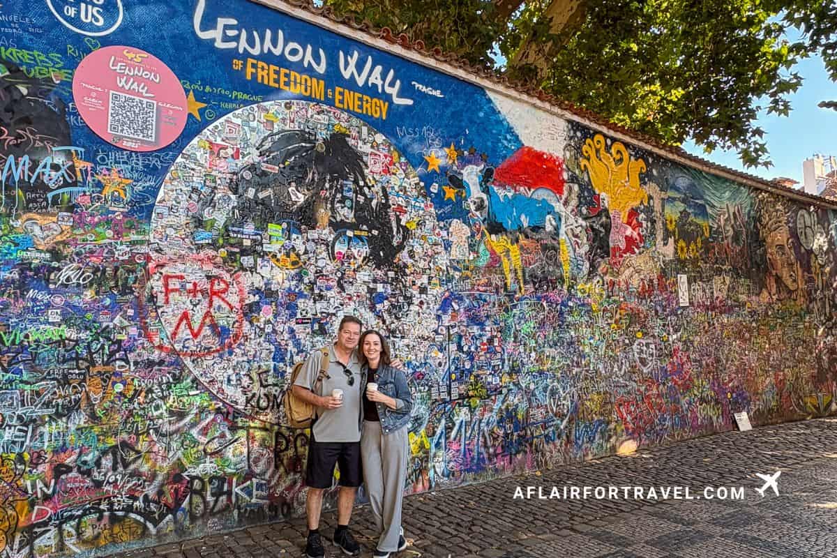 Couple posing in front of the colorful John Lennon Wall in Prague, covered in vibrant graffiti art, peace messages, and Beatles-inspired murals in Malá Strana