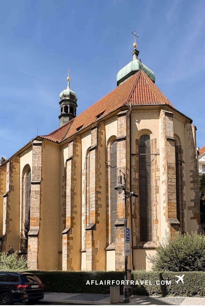 Church of Our Lady Victorious in Prague with terracotta tile roof, green copper domes, baroque architecture, and tall arched windows against blue sky, which you can view the exterior for free