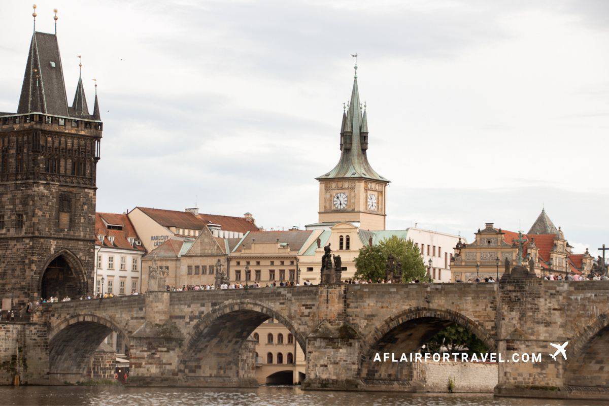 Charles Bridge, one of the best free things to see in Prague, spanning the Vltava River in Prague with medieval Gothic towers, stone arches, clock tower, and historic buildings along the riverbank