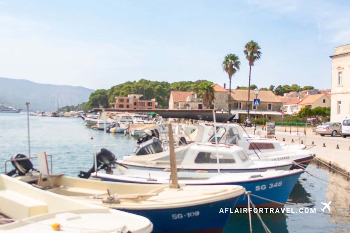 Traditional fishing boats moored in Stari Grad harbor on Hvar Island, Croatia, with palm trees, colorful Mediterranean buildings, and forested hills in the background