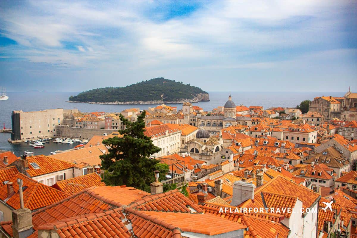 Aerial view of Dubrovnik's Old Town with iconic orange terracotta roofs, baroque cathedral dome, medieval stone fortifications, historic harbor, and forested Lokrum Island in the Adriatic Sea beyond is one of the reasons it's worth visiting Croatia