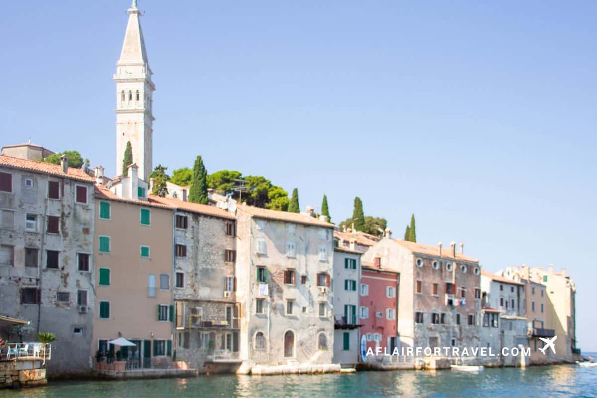 Colorful Venetian-style buildings rising directly from the Adriatic Sea in Rovinj old town, Croatia, with distinctive white bell tower and cypress trees on the hillside