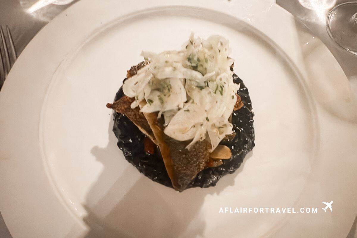 Gourmet plated seafood dish with black squid ink risotto and fresh fish at fine dining restaurant in Cap Maison