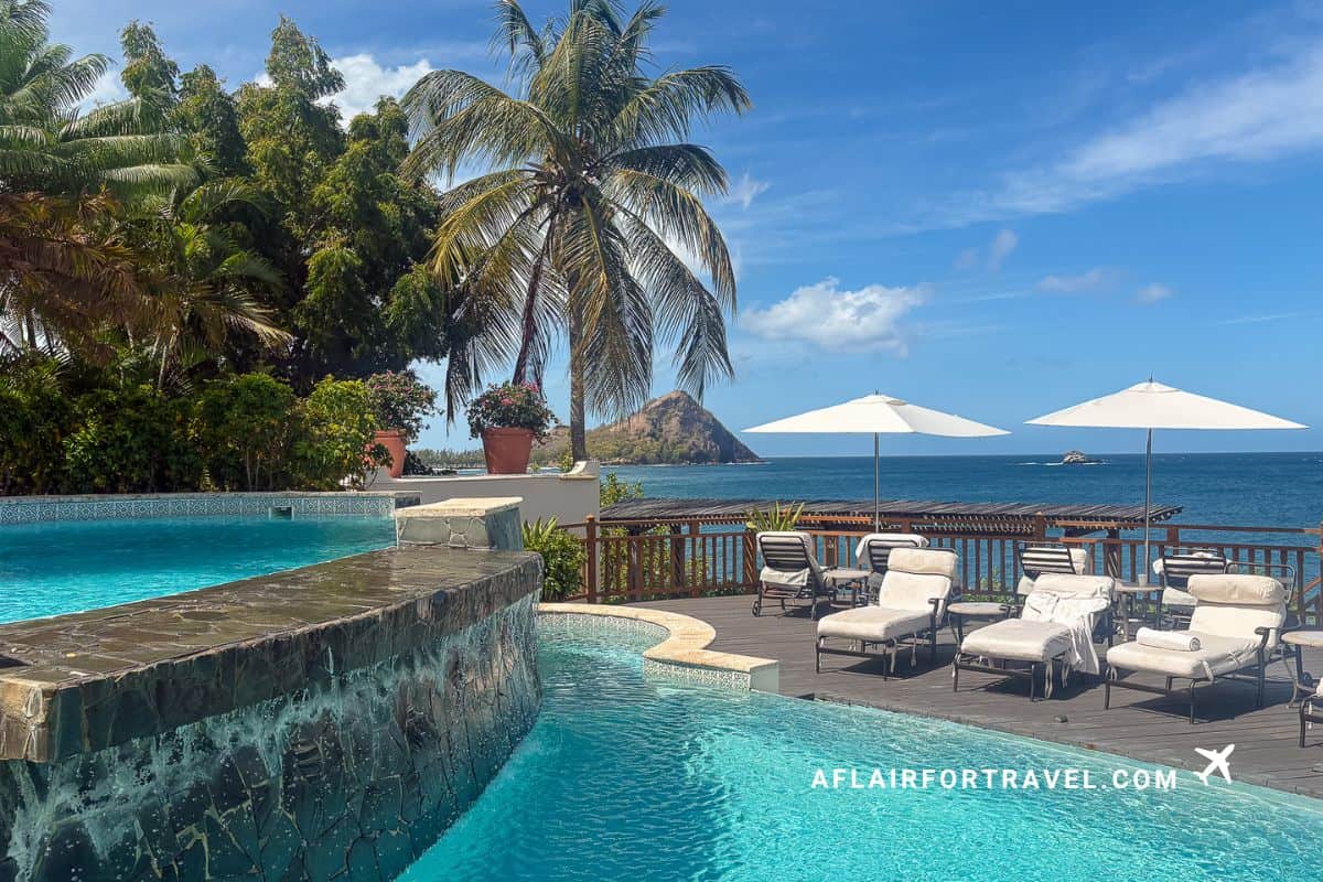 Multi-level infinity pools surrounded by palm trees with white umbrellas and loungers overlooking Caribbean Sea at Cap Maison