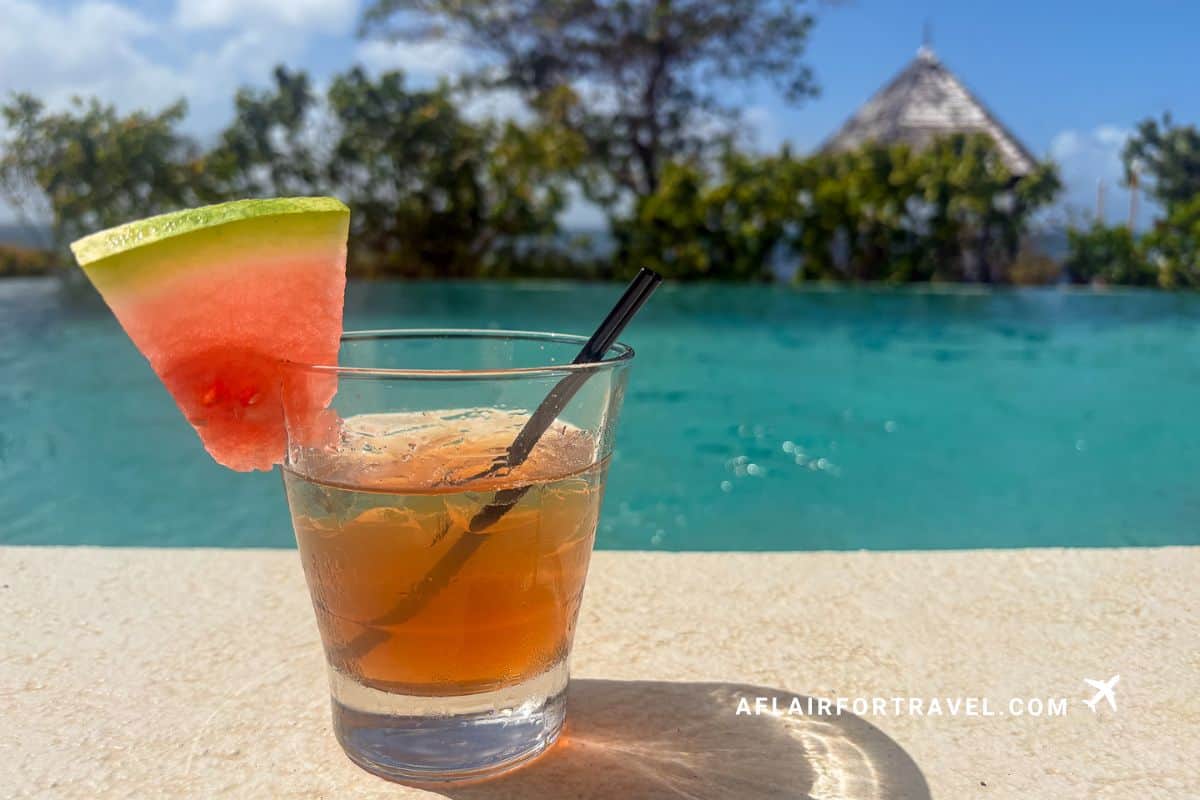 Signature rum punch with watermelon garnish beside turquoise infinity pool is a great reason to stay at Cap Maison St. Lucia