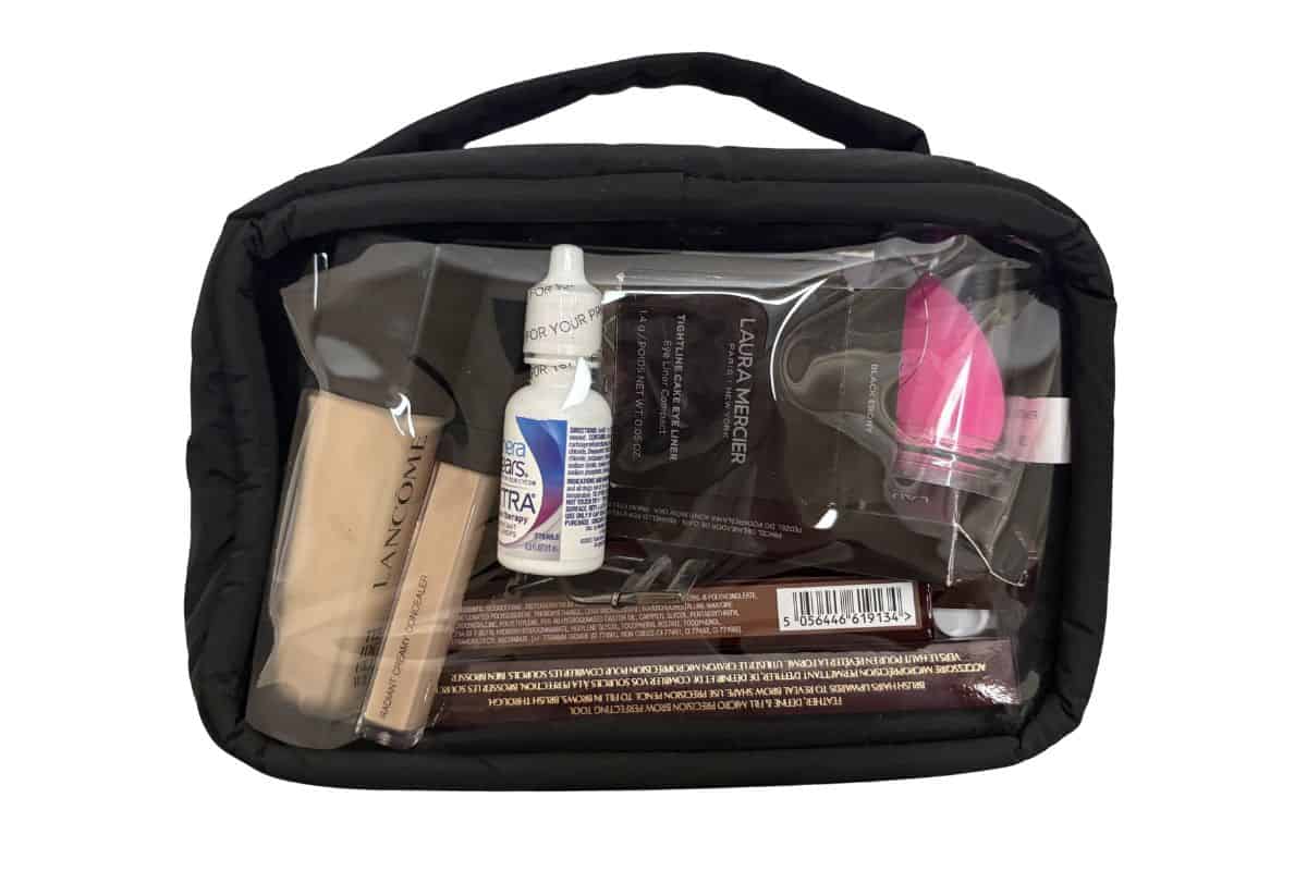 Clear TSA-compliant toiletry bag filled with travel-size beauty products including Lancôme foundation, Laura Mercier powder, beauty blender, and skincare items for airport security