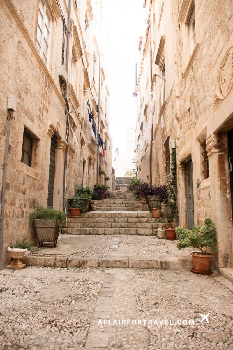 Narrow stone stairway in Dubrovnik Old Town lined with limestone buildings, terracotta planters, and Mediterranean plants along cobblestone streets, one of many stairways in Old Town that visitors should know about