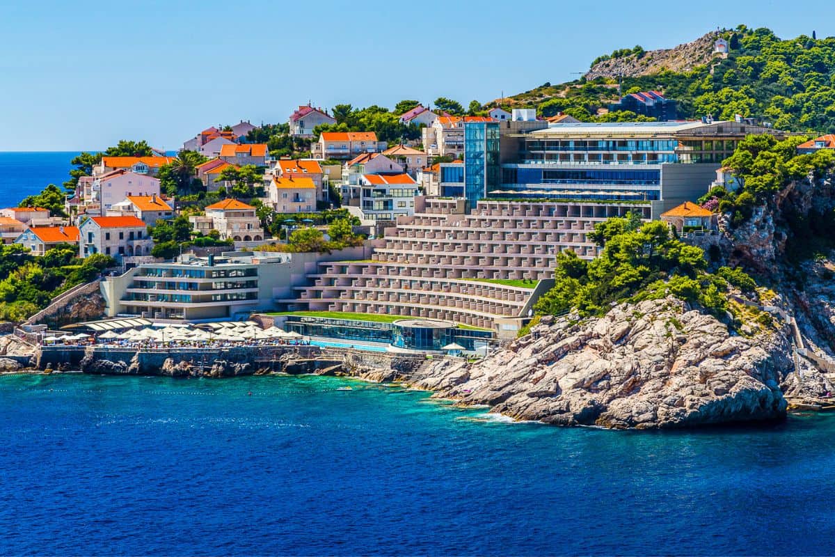 Luxury cliffside hotel Dubrovnik perched above turquoise Adriatic waters with rocky coastline and traditional terracotta-roofed buildings on hillside
