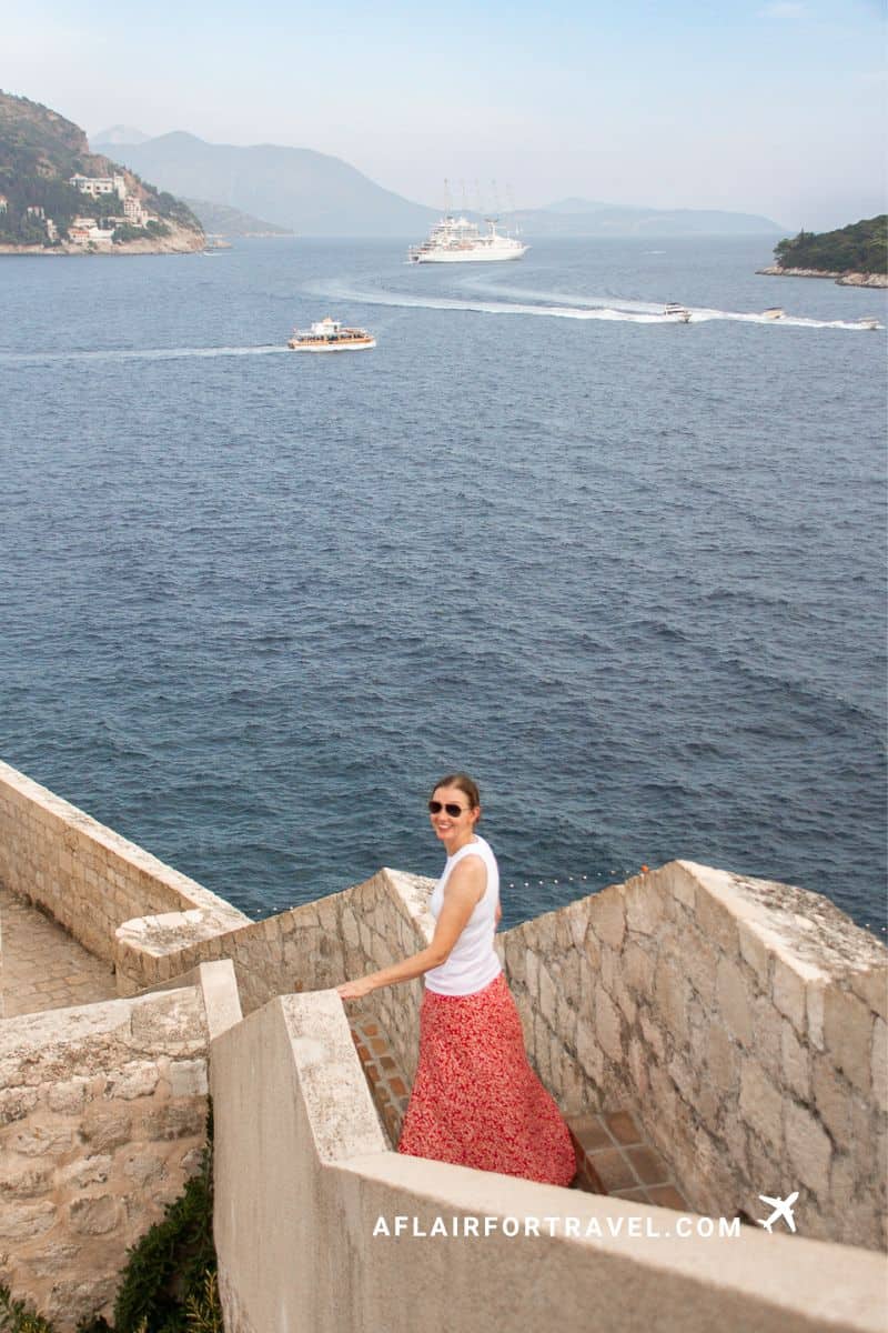 Woman descending stone steps on Dubrovnik's city walls with cruise ships on the Adriatic Sea in the background, a scenic highlight of a 3-day Dubrovnik itinerary