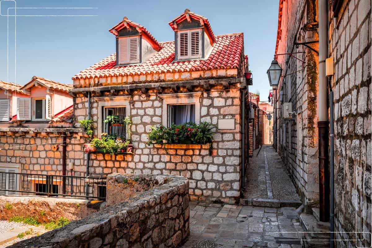 Charming cobblestone alley lined with traditional stone houses, flower-filled window boxes, and terracotta rooftops in Dubrovnik's Old Town
