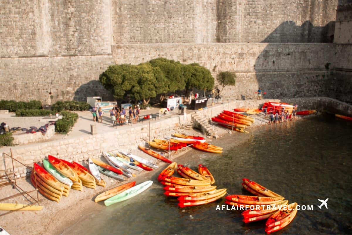 Colorful kayaks lined up along Dubrovnik’s stone city walls with people preparing for a coastal paddle, a popular tour on a 3 day Dubrovnik itinerary