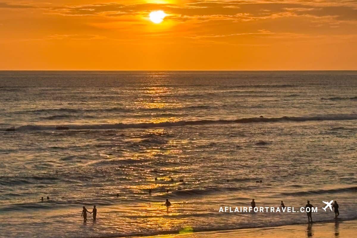 Sunset over the Pacific Ocean in Costa Rica with people swimming, and walking along the shoreline.