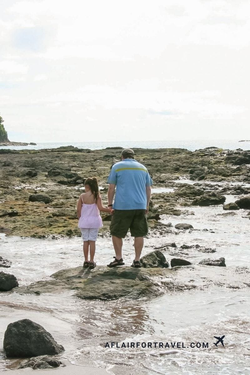 Family exploring a rocky beach in Costa Rica during low tide, showing the importance of timing and proper footwear