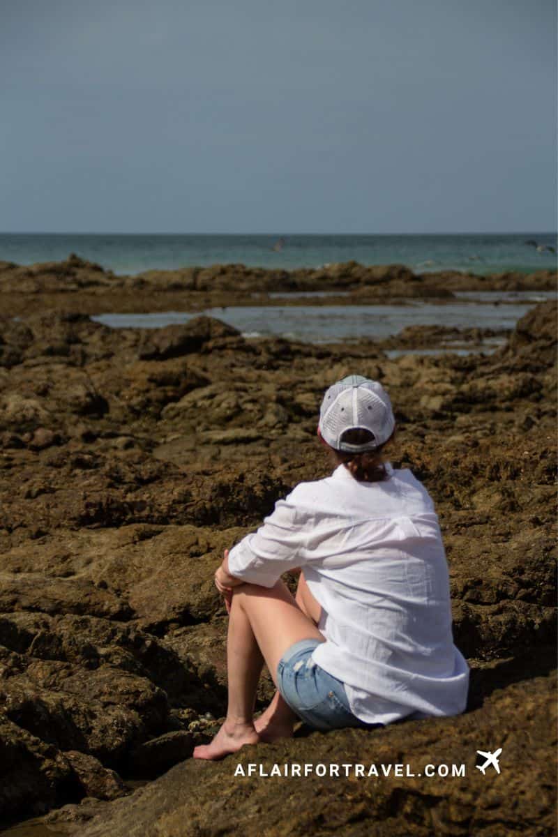 Traveler sitting on rocky shoreline in Costa Rica, enjoying a quiet coastal moment away from crowds